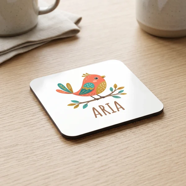 Personalised square coaster on a table with a bird illustration and name design.